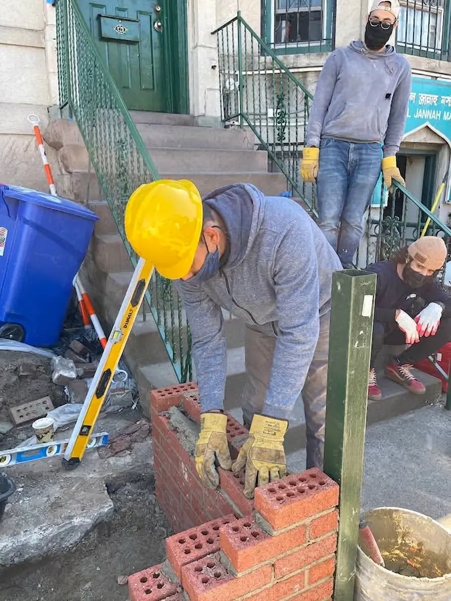 Mr. Tipu, our founder, in a yellow hard hat laying bricks while two crew members watch
